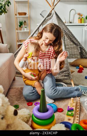 Eine junge Mutter spielt glücklich mit ihrer Kleinkind-Tochter in einem gemütlichen Zimmer und baut eine liebevolle und freudige Verbindung auf. Stockfoto