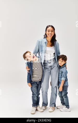 Eine junge asiatische Mutter und ihre kleinen Söhne, alle in Denim-Outfits gekleidet, posierten zusammen für ein Porträt in einem grauen Studio. Stockfoto