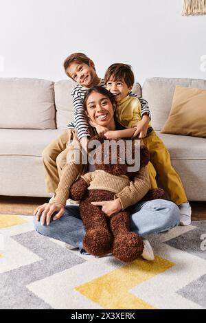 Eine junge asiatische Mutter sitzt auf dem Boden mit ihren zwei kleinen Söhnen und einem Teddybären und genießt einen friedlichen Moment zusammen. Stockfoto