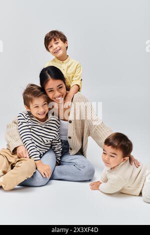 Eine junge asiatische Mutter sitzt auf dem Boden und umschließt ihre Kinder in einem ruhigen und liebevollen Moment. Stockfoto