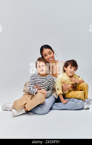 Eine junge asiatische Mutter sitzt mit ihren beiden Kindern friedlich auf dem Boden in einem Studio auf grauem Hintergrund. Stockfoto