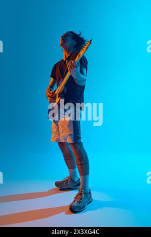 Bühnenlichter beleuchten den leidenschaftlichen Auftritt des jungen Musikers mit elektrischer Gitarre vor blauem, cyanfarbenem Hintergrund im Neonlicht Stockfoto