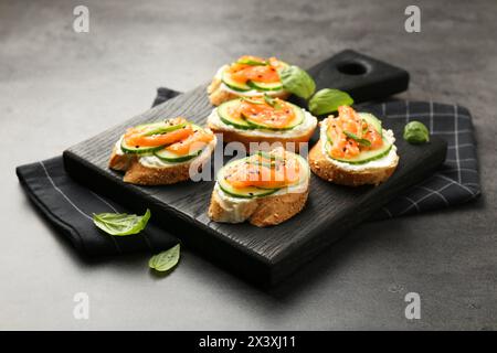 Leckere Kanapees mit Lachs, Gurke und Frischkäse auf grauem Tisch Stockfoto