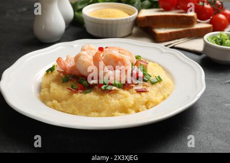 Teller mit frischen, leckeren Garnelen, Speck, Grütze, grünen Zwiebeln und Pfeffer auf schwarzem Tisch, Nahaufnahme Stockfoto