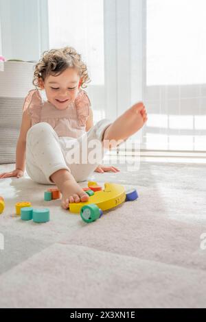 Vertikales Foto eines lächelnden Mädchens beim Spielen mit bunten, nachhaltigen Holzstücken. montessori-Materialien. Entwicklung und Lernen Stockfoto