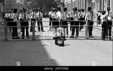 London, Großbritannien. Juni 1984. Ein einsamer, gewaltfreier Aktivist sitzt vor einer Polizeilinie in der Nähe des Eingangs zum Grosvenor Square, London, 9. Juni 1984. Die Aktion war eine Reaktion auf den Besuch des amerikanischen Präsidenten, Ronald Reagans auf dem Weltwirtschaftsgipfel in London und die Stationierung von US-amerikanischen Kreuzfahrtraketen in Großbritannien. Der Protest fiel zeitlich mit der Anti-Cruise-Raketenkundgebung des CND auf dem Trafalgar Square zusammen. London. Der Grosvenor Square war zum Zeitpunkt des Protestes der Sitz der amerikanischen Botschaft in Großbritannien. Stockfoto