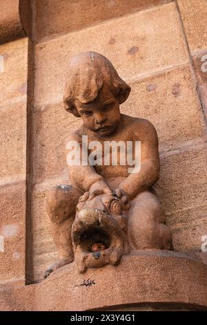 Verfaulter Apfel im Mund eines Fisches, Skulptur eines kleinen Jungen an der Außenfassade des Südtiroler Archäologischen Museums, Bozen, Italien. Stockfoto