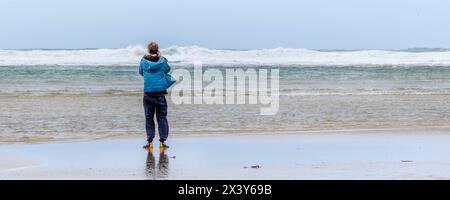 Ein Panoramablick von hinten eines Mannes, der die eintretende Flut am Crantock Beach in Newquay in Cornwall in Großbritannien fotografiert. Stockfoto