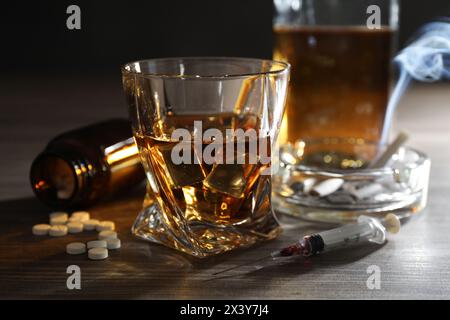 Alkohol- und Drogensucht. Whiskey in Glas, Spritze, Pillen und Zigaretten auf Holztisch Stockfoto