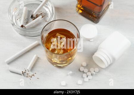 Alkohol- und Drogensucht. Whiskey in Glas, Zigaretten und Pillen auf weißem Tisch Stockfoto