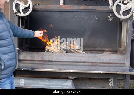 Ein Mann steht in der Nähe eines riesigen professionellen Barbecue und wärmt sich an einem Herbsttag die Hände. Stockfoto