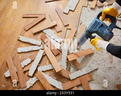 Parkett aus Holz auf der Platte verklebt, entfernt mit einem elektrischen Abbruchhammer von einem Handwerker in Arbeitskleidung, in der Wohnung, die gerade renoviert wird. In der Zukunft Stockfoto