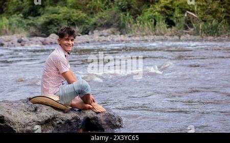 Lifestyle. Lächelnder Mann, der auf einem Felsen im Fluss sitzt Stockfoto