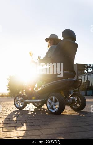 Frau, die auf einer Straße in der Stadt einen Elektroroller mit vier Rädern fährt. Stockfoto