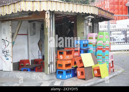 Stapel leerer Getränkeflaschenkisten und Stapel kurzer Plastikstühle in einem alten Laden am Straßenrand Stockfoto