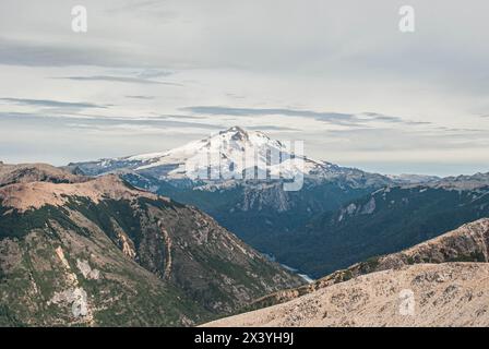 Weitläufiger Blick auf den schneebedeckten Berg Tronador, umgeben von zerklüfteten Hügeln und Wäldern unter einem bewölkten Himmel in patagonien, argentinien Stockfoto