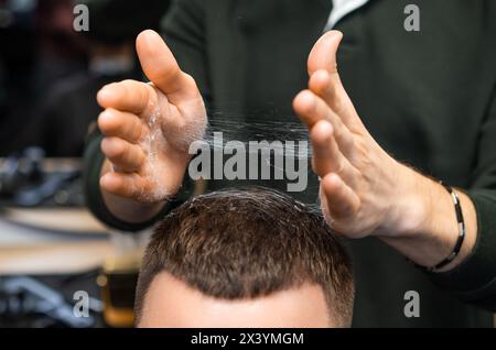 Friseur passt frisch geschnittene Haare des Kunden in der Nähe des Friseurs an. Ein sorgfältiger Stylist zerzaust einen Friseurdiener im Friseursalon Stockfoto