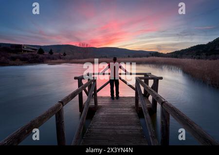 Ein Mann mitten auf einem Holzsteg, der die Ruhe einer Lagune bei Sonnenuntergang genießt Stockfoto