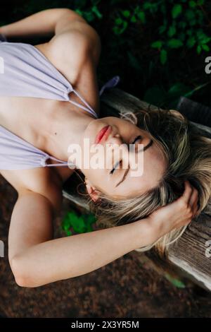 Ein wunderschönes Teenager-Mädchen, das im Wald liegt, mit der Hand am Kopf Stockfoto