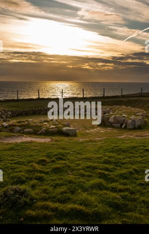 Dinas Dinlle grub Überreste eines eisenzeitlichen Hauses aus, als die Sonne über dem irischen Meer unterging. Dinas Dinlle liegt an der Nordwales Küste in Gwynedd. Stockfoto