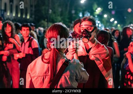 Tiflis, Georgien. April 2024. Zwei junge Frauen, die in georgische Fahnen gehüllt und Gasmasken tragen, halten die Hände bei einem Protest gegen die Wiedereinführung eines Gesetzes über "ausländische Agenten" in Zentral-Tiflis. Quelle: SOPA Images Limited/Alamy Live News Stockfoto