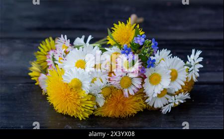 Blumenstrauß aus Sommerwildblumen, Gänseblümchen, Vergissmeinnots, Löwenzahn auf hölzernem Hintergrund Stockfoto