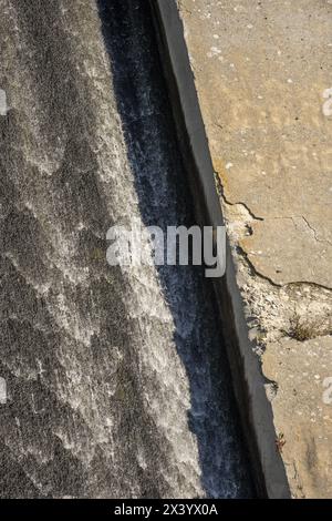 Eine Betonrampenoberfläche mit einigen Schäden, um Wasser aus einem Damm voller Unkraut und Algen zu evakuieren Stockfoto