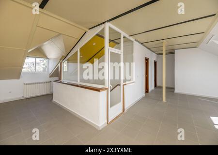 Großes Dachgeschoss mit einer Metallsäule in der Mitte, verglaste Treppe, eine Wand mit Regalen und ein leeres Badezimmer Stockfoto