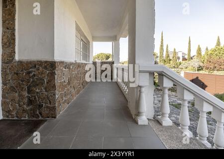 Weiße Balustraden einer langen Terrasse Außenterrasse eines Einfamilienhauses mit Zugang zur Haupttür des Hauses mit grauem Terrazzo-Boden Stockfoto