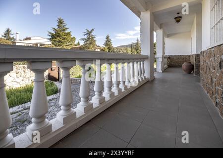 Blick auf die Gärten eines Hauses mit weißen Brüstungen von einer langen Außenterrasse mit dekorativem Tongefäß Stockfoto