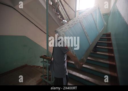 CHARKIW, UKRAINE - 27. APRIL 2024 - Männer tragen eine Glaseinheit die Treppe hinauf im Psychiatrischen Krankenhaus N3 im Bezirk Saltivskyi, um ein kaputtes Fenster nach einem nächtlichen russischen S-300-Raketenangriff in Charkiw, Nordostukraine zu ersetzen. Am 27. April um 00:30 Uhr Ortszeit griffen russische Truppen das Psychiatrische Krankenhaus N3 in Charkiw mit S-300-Luftabwehrraketen an. Fenster, Dach, nicht genutztes Gebäude, Lebensmittelblock, Heizraum und andere Gebäude wurden beschädigt. Eine 53-jährige Frau wurde verletzt. Während des Streiks waren 60 Patienten und 5 Krankenhausmitarbeiter anwesend. Stockfoto