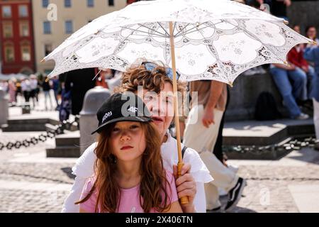 Krakau, Polen. April 2024. Eine Frau mit einem Mädchen, leicht gekleidet unter einem Schirm auf einem Hauptmarkt in der Altstadt von Krakau, als eine Hitzewelle in Polen eintrifft, die fast 30 Grad Celsius erreicht - sehr ungewöhnliche Temperatur für April. Quelle: SOPA Images Limited/Alamy Live News Stockfoto