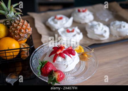 Meringue mit Erdbeeren auf einem klaren Teller, Obst im Hintergrund. Ideal für Rezeptblogs. Hochwertige Fotos Stockfoto