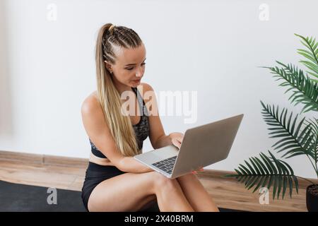 Junge Frau in Fitnesskleidung mit Laptop auf Yogamatte Stockfoto