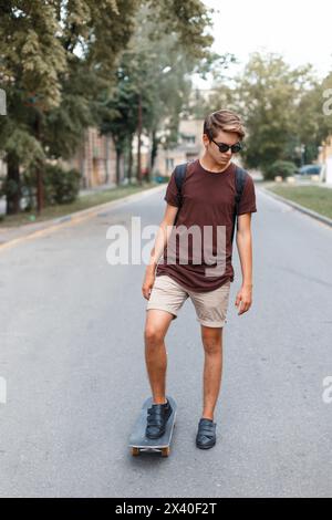 Junger gutaussehender Kerl in Sonnenbrille, der auf Einem Skateboard fährt. Stockfoto