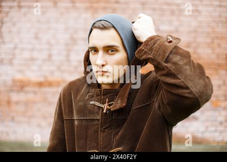 Der junge, stilvolle Mann trägt Eine Haube auf dem Hintergrund der roten Ziegelmauer Stockfoto