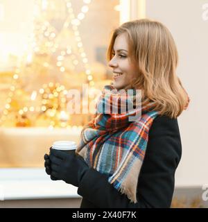 Hübsche Frau Mit Kaffee In Der Hand Geht Auf Dem Hintergrund Der Gelben Lichter Stockfoto