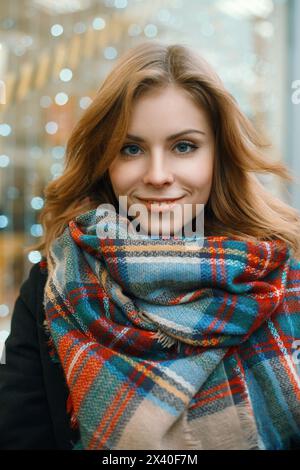 Nahaufnahme Porträt Einer schönen Frau in Einem stilvollen Retro-Schal und schwarzem Mantel auf dem Hintergrund von Vitrinen mit Lichtern Stockfoto