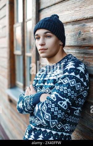 Junger Mann In Stilvoller Strickkleidung, Der Neben Der Holzwand Steht Stockfoto