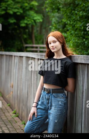 Rothaariges zwölfjähriges Mädchen mit Sommersprossen, das sich an einen Zaun lehnt, Jette, Belgien. Modell freigegeben. Stockfoto