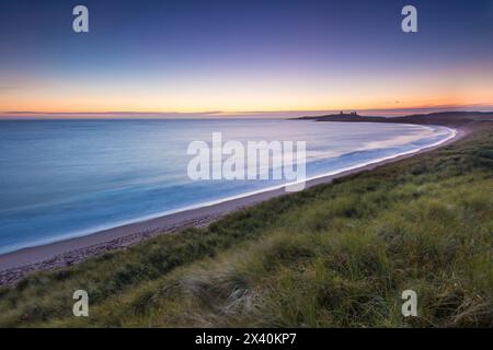 Embleton Beach bei Sonnenaufgang mit Dunstanburgh Castle in der Ferne; Northumberland, England, Vereinigtes Königreich Stockfoto