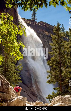 Blick von hinten auf einen Wanderer mit Blick auf die Vernal Falls an einem sonnigen Tag; Yosemite National Park, Kalifornien, Vereinigte Staaten von Amerika Stockfoto