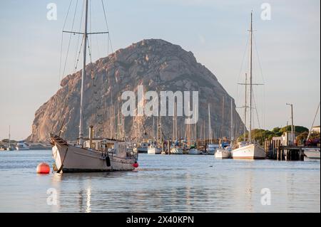 Warmes Sonnenlicht reflektiert auf den Fischerbooten, die im Hafen der Morro Bay Lagoon mit Morrow Rock im Hintergrund liegen Stockfoto