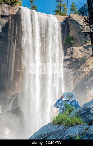 Blick von hinten auf einen Wanderer mit Blick auf die Vernal Falls an einem sonnigen Tag; Yosemite National Park, Kalifornien, Vereinigte Staaten von Amerika Stockfoto