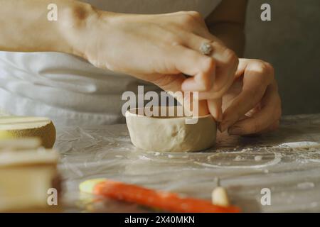 Eine Frau formt eine graue Tonplatte mit ihren Händen, Nahaufnahme. Basteln aus Lehm. Hobbys und Kreativität. Stockfoto