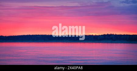 Der Abendhimmel entzündet sich mit Farbe, während die Sonne unter der Horizontlinie in Fort Simpson untergeht. Der Mackenzie River reflektiert die Farbe in einem wunderschönen ... Stockfoto