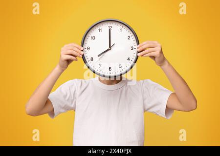 Teenager, der sein Gesicht mit großer Uhr bedeckt, orangefarbenes Panorama Stockfoto