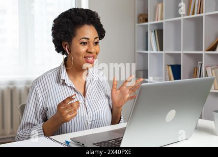 Eine junge Afrikanerin spricht, während sie bei einer Videokonferenz oder einem Webinar auf den Laptop schaut. Online-Schulung. Stockfoto