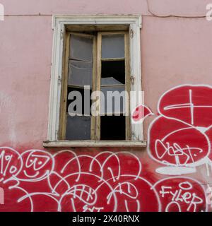 Graffiti und kaputtes Fenster an der Seite eines Gebäudes; Athen, Griechenland Stockfoto