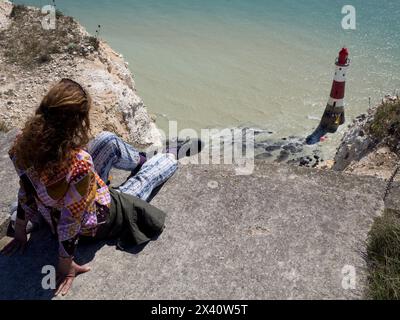 Frau, die von einem Aussichtspunkt aus auf den Leuchtturm von Beachy Head und das Meer blickt, Beachy Head, East Sussex, Großbritannien; Eastbourne, East Sussex, England Stockfoto